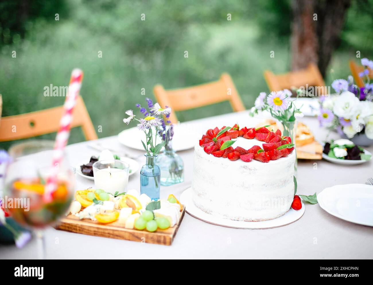 Gustosa torta con frutti di bosco posta sul tavolo da banchetto vicino a fiori e stoviglie il giorno d'estate in giardino Foto Stock