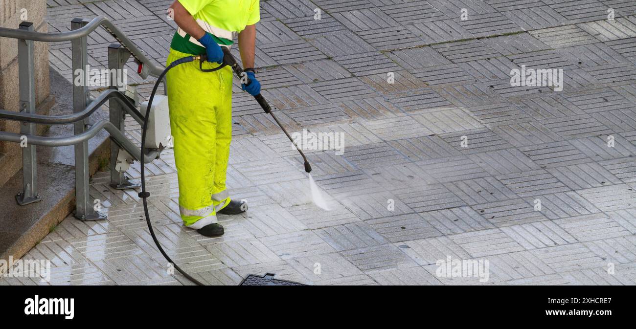 Operaio che pulisce un marciapiede di strada con getto d'acqua ad alta pressione. Concetto di manutenzione urbana. Spazio di copia Foto Stock