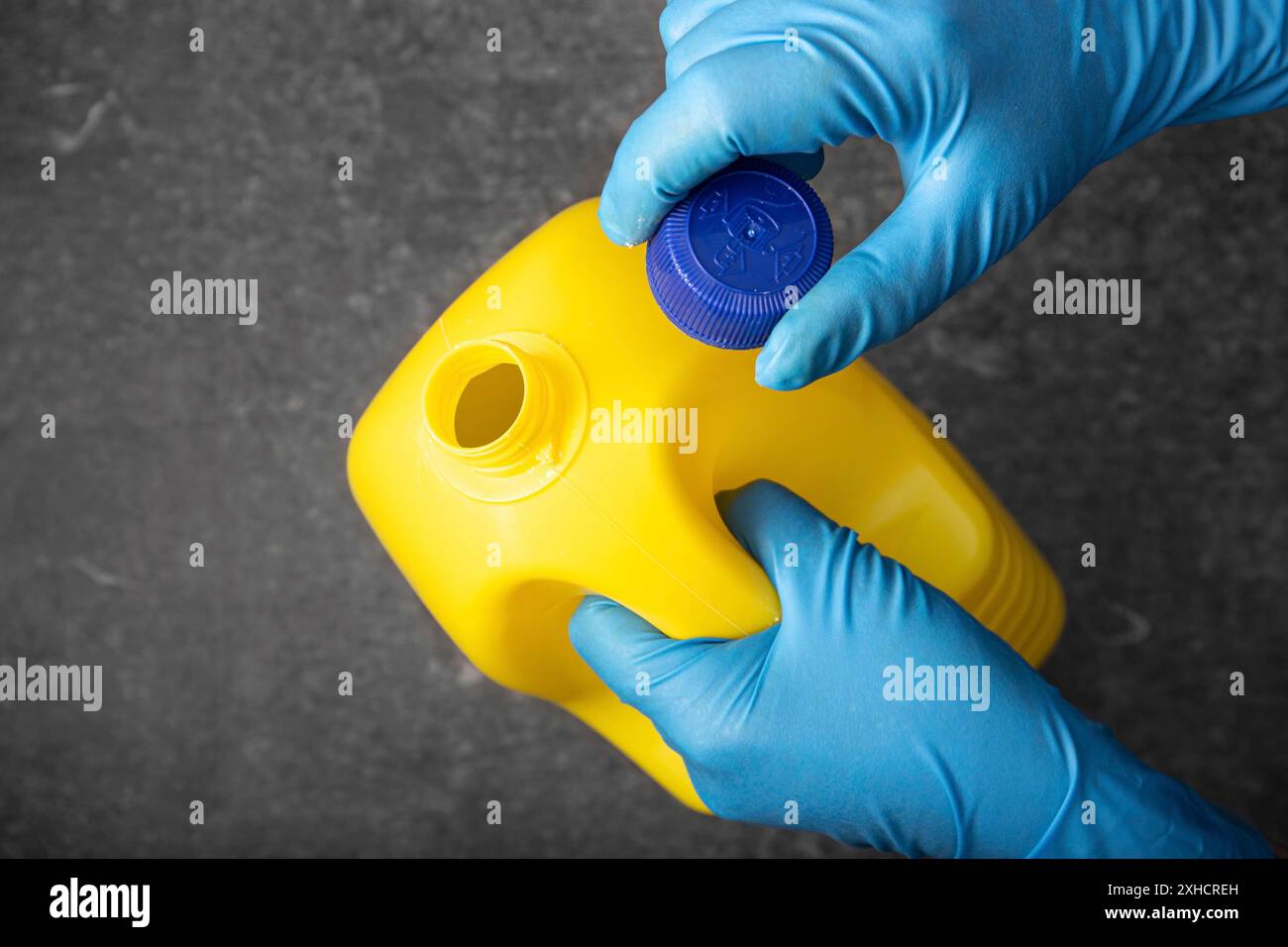 Mano umana in un guanto protettivo che apre un flacone di candeggina giallo. Concetto di disinfezione Foto Stock