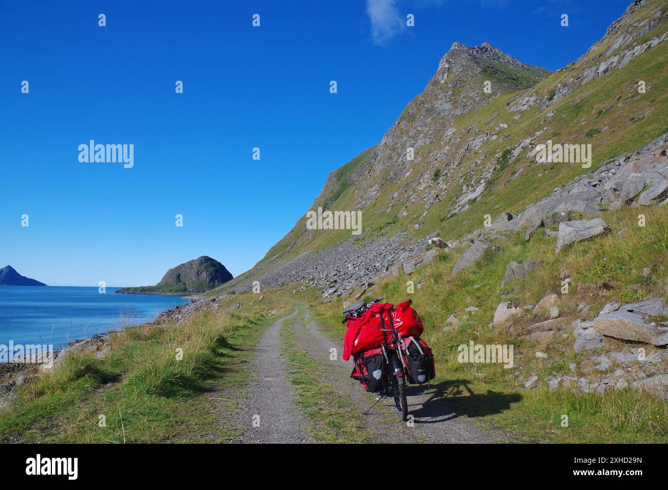 In bicicletta su una strada ghiaiosa lungo il mare con vista sulle montagne e sul cielo azzurro, vacanze in bicicletta, vacanze avventurose, Haukland, Leknes Foto Stock