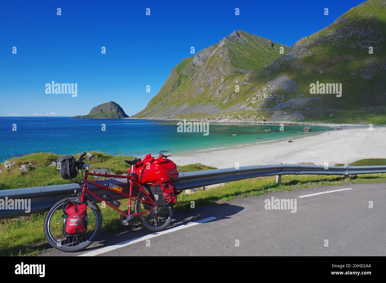 Bicicletta con sacchi rossi su una strada lungo una spiaggia con acqua turchese, in mezzo alle montagne e al cielo azzurro, tour in bicicletta, vacanze avventurose Foto Stock