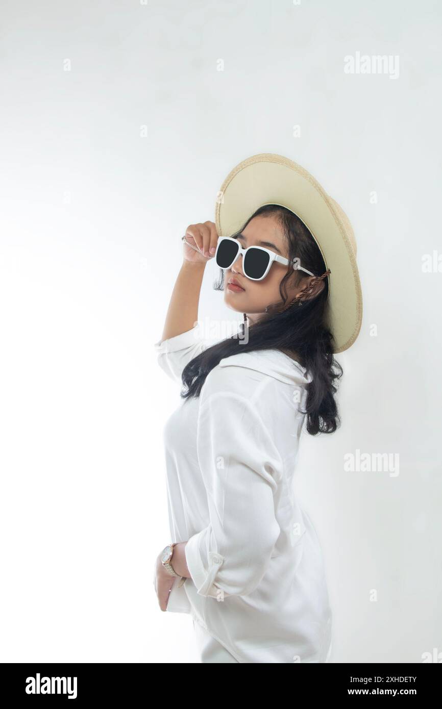 Ritratto di una bella giovane donna asiatica in abiti bianchi casual con cappello di paglia e occhiali da sole isolati su sfondo bianco. Concetto di vacanza estiva Foto Stock