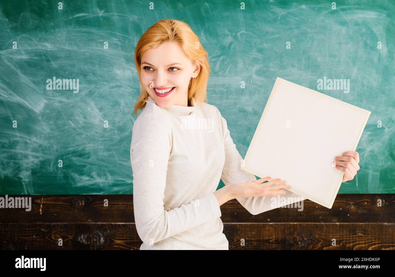 Torna a scuola. Ritratto di un insegnante sorridente con libro in classe in classe. Istruzione, apprendimento e conoscenza. Studentessa con libro vicino al nero Foto Stock