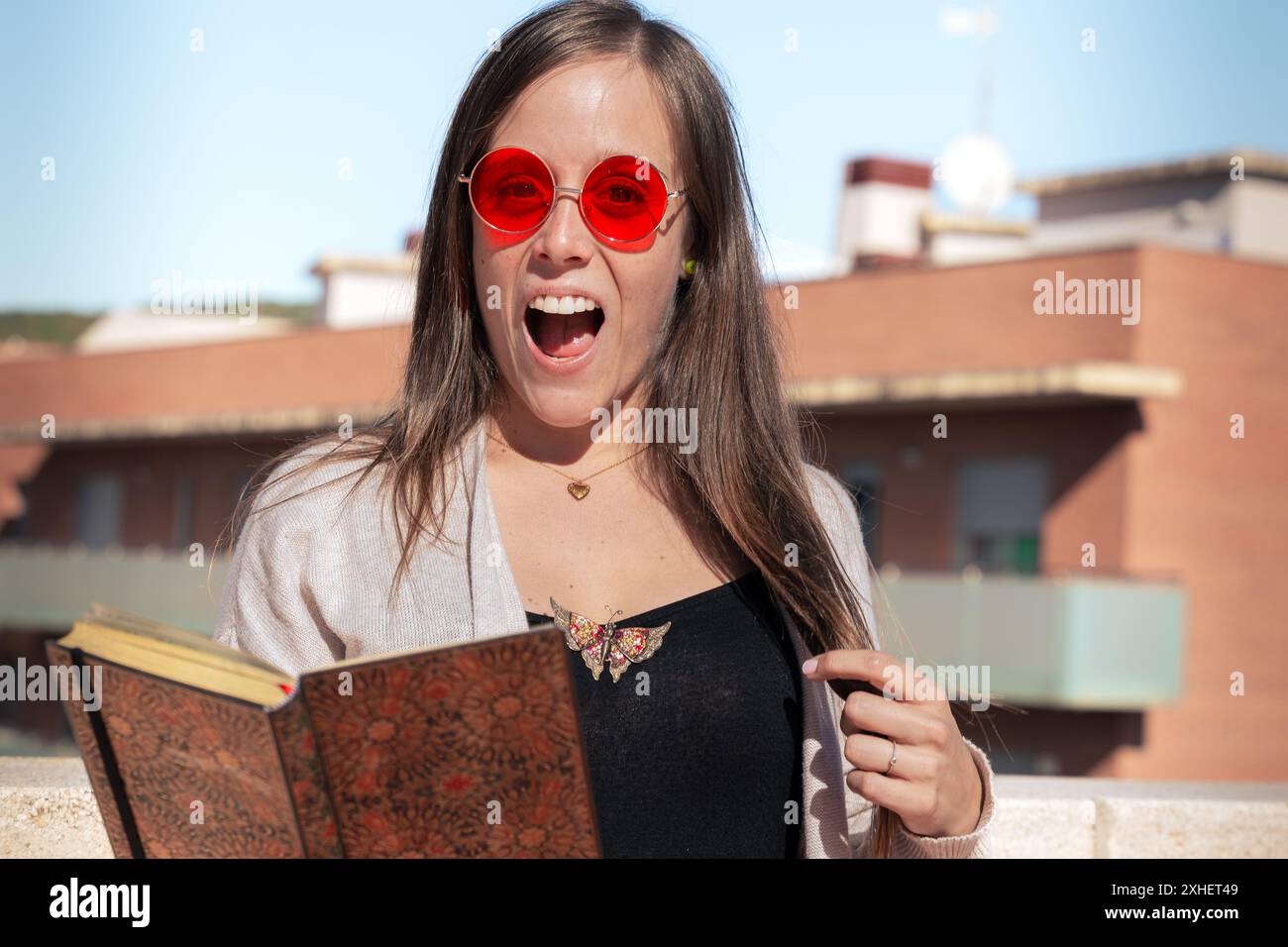 Giovane donna felice che legge un libro con il caffè in mano all'aperto Foto Stock