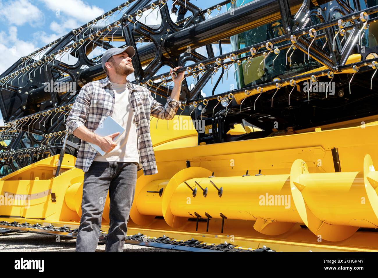 Uomo adulto caucasico con tavoletta digitale in mano che guarda una mietitrebbia gialla presso un rivenditore di macchinari agricoli. Rivenditore o fornitore di attrezzature AG. Foto Stock