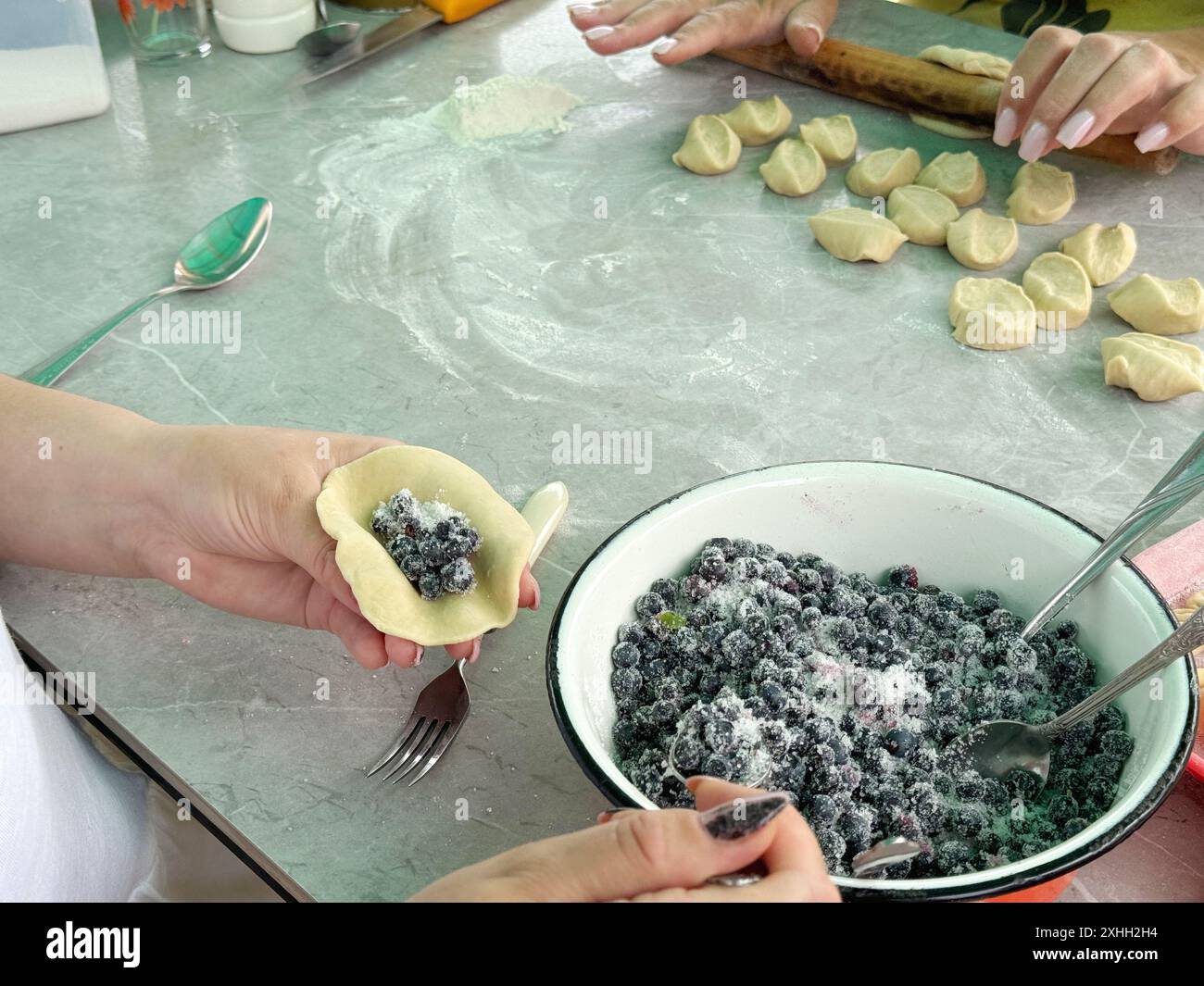 Le donne preparano gnocchi con mirtilli. Uno riempie l'impasto arrotolato di frutti di bosco. Un'altra stende l'impasto. Foto Stock