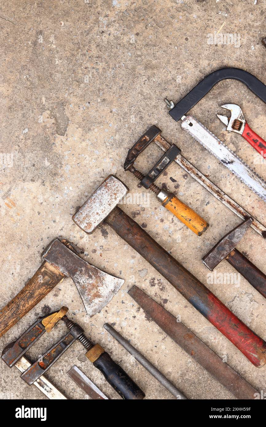 Vecchi strumenti da costruzione disposti su uno sfondo in cemento, vista dall'alto. Martello, morsetto per edilizia, lima piatta, martello, sega a mano e pinze. Collezionisti Foto Stock