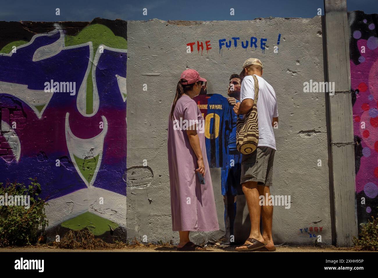 Barcellona, Spagna. 14 giugno 2024. I pendolari ispezionano il nuovo murale dell'artista urbano italiano "TVBoy", Salvatore Benintende. Intitolato "il futuro", i graffiti raffigurano Lionel messi in possesso di una maglia del FC Barcelona con il suo ex numero 10 e il nome Lamine Yamal, presentando la giovane stella il giorno in cui potrebbe diventare il più giovane vincitore di un campionato europeo di UEFA, come suo successore. Crediti: Matthias Oesterle/Alamy Live News Foto Stock