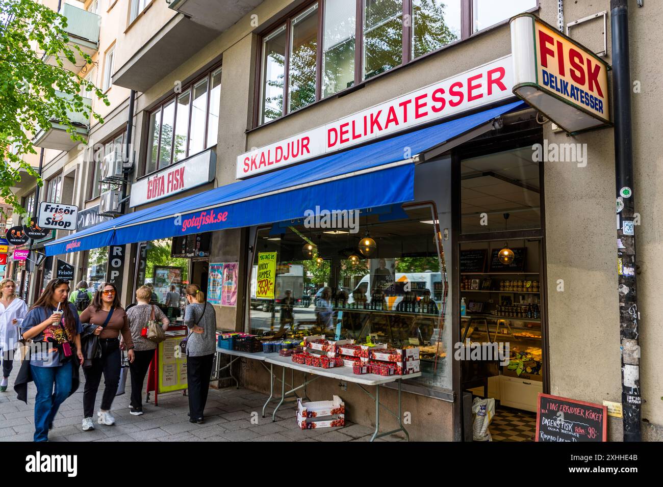 I cartelli "Fisk Delikatesser" e "Skaldjur Delikatesser" (delicatessen di frutti di mare) segnano la pescheria Göta Fisk su Götgatan a Södermalm, Stoccolma, un pescatore popolare dagli anni '60. Un negozio di pescheria occupa il piano terra qui dalla costruzione dell'edificio nel 1932. I passanti passano davanti alla vetrina delle casse all'esterno. Götgatan, Södermalm, Stoccolma, Contea di Stoccolma, Svezia. Foto Stock