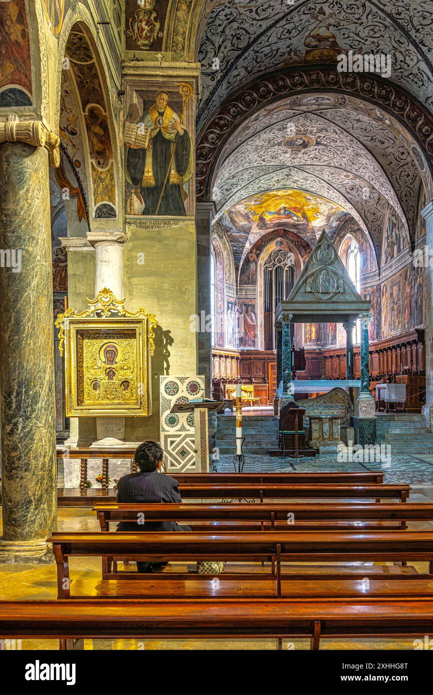 Il ciborio, gli archi e le colonne riccamente decorate dell'Abbazia di Farfa. Una donna che prega davanti all'icona mariana di ispirazione orientale. Lazio Foto Stock