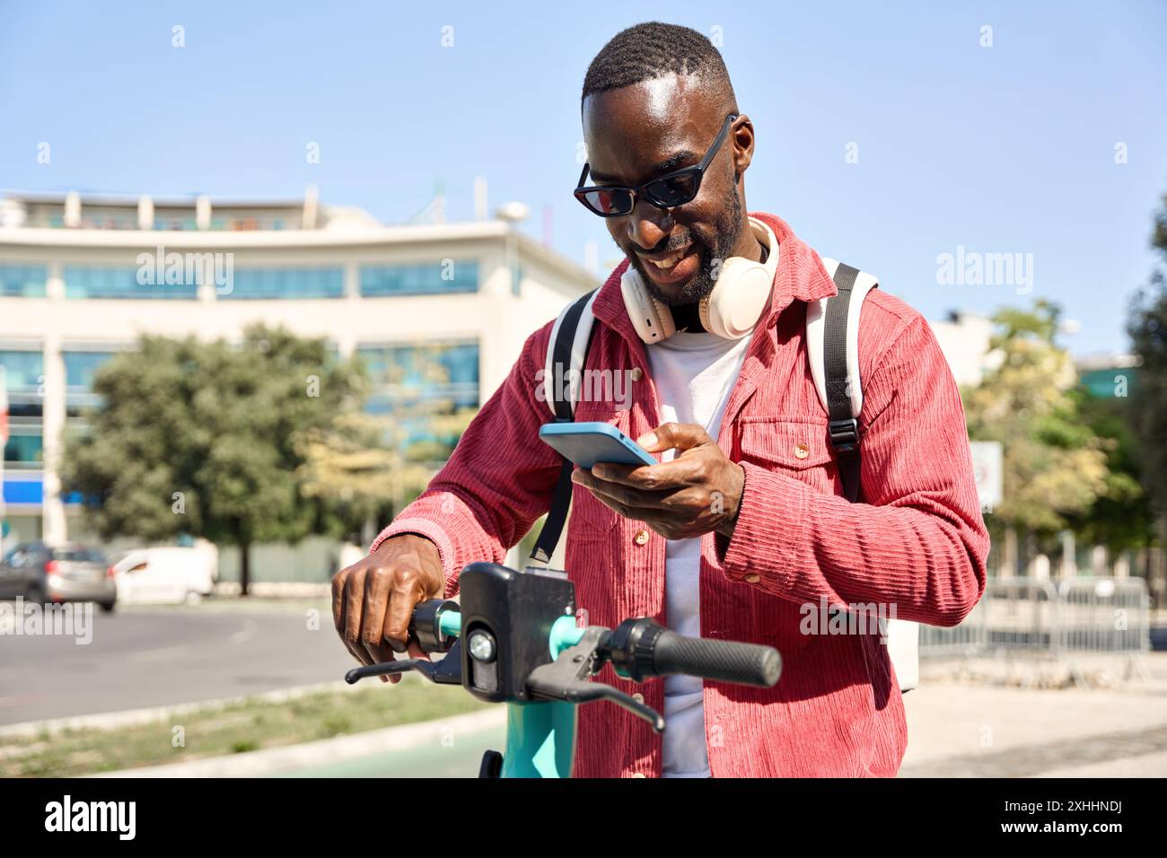 Felice giovane africano uomo turista che guida scooter elettrico bici utilizzando il telefono. Foto Stock