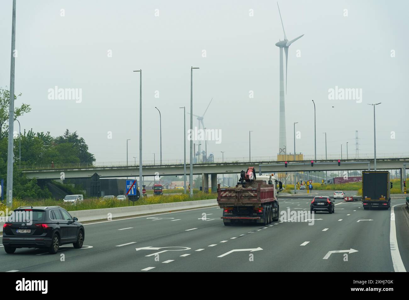 Gent, Belgio - 22 maggio 2023: Due auto stanno percorrendo un'autostrada costeggiata da turbine eoliche. I veicoli sono circondati da grandi fonti di energia rinnovabile Foto Stock