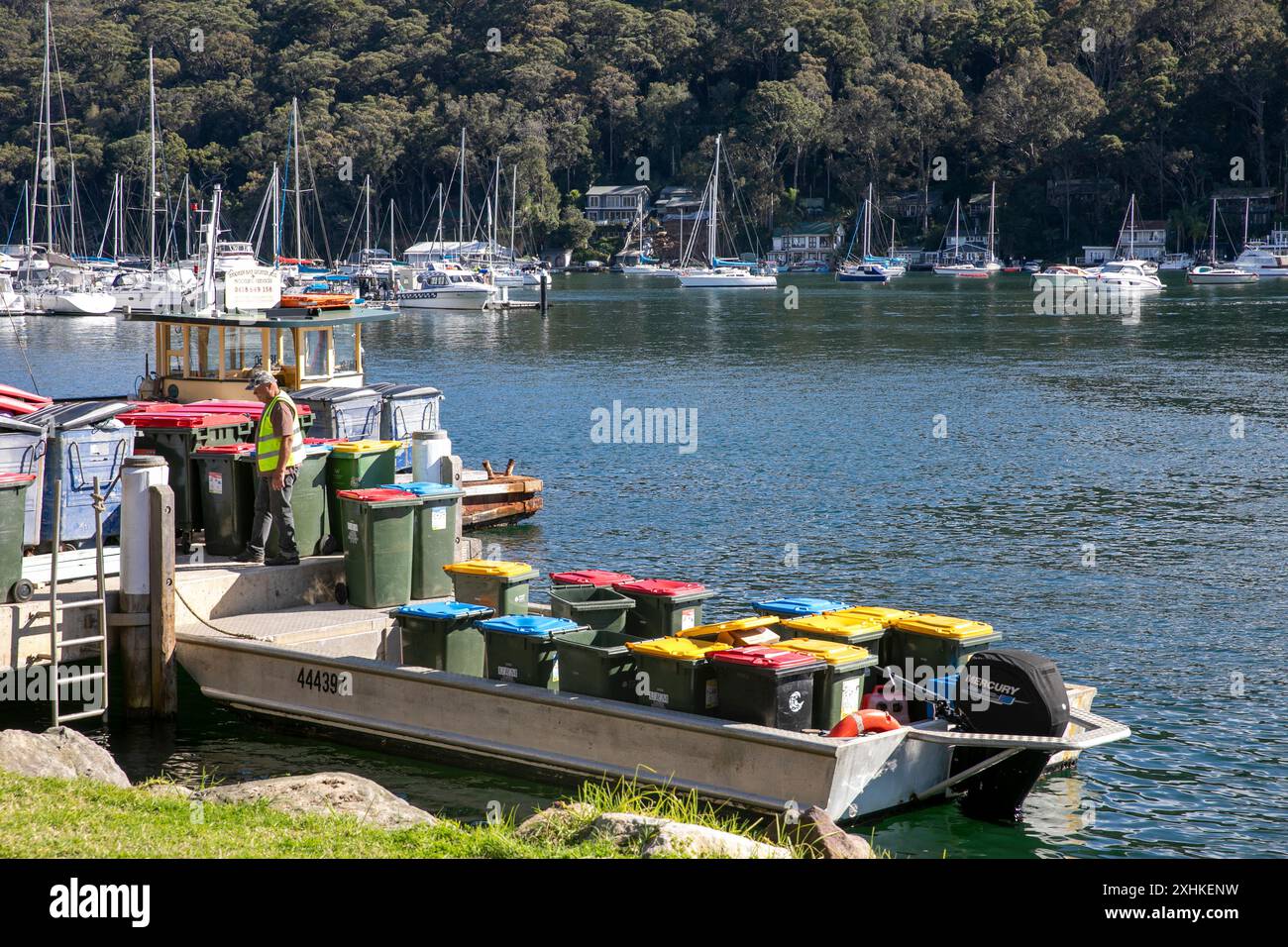 Raccolta rifiuti, barchetta rimuove i contenitori domestici da Scotland Island a Church Point sulla terraferma, Sydney, NSW, Australia Foto Stock