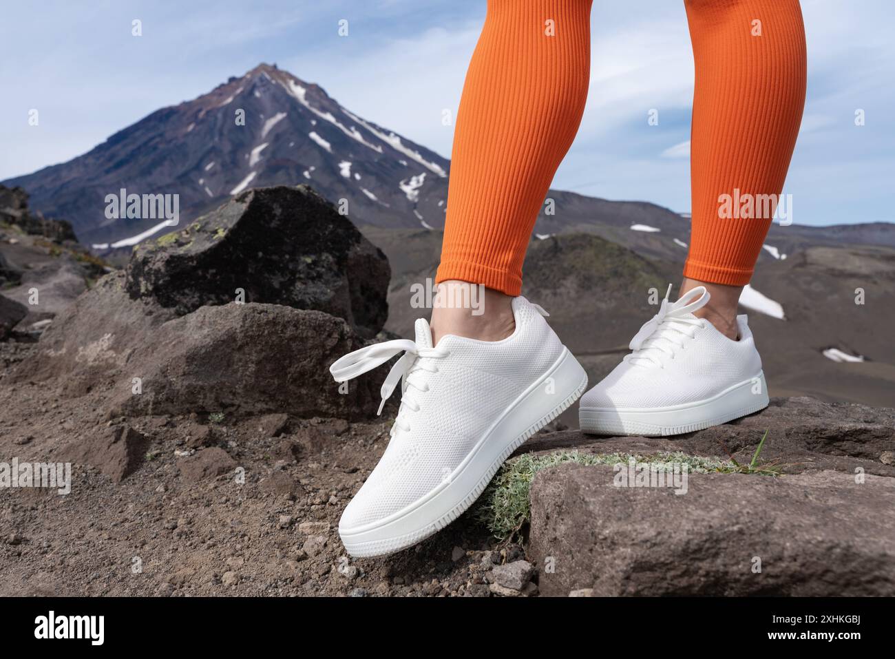 Vista ravvicinata delle gambe della donna che indossano scarpe da ginnastica bianche e leggings sportivi arancioni. Donna in piedi durante l'allenamento in montagna con una splendida vista Foto Stock