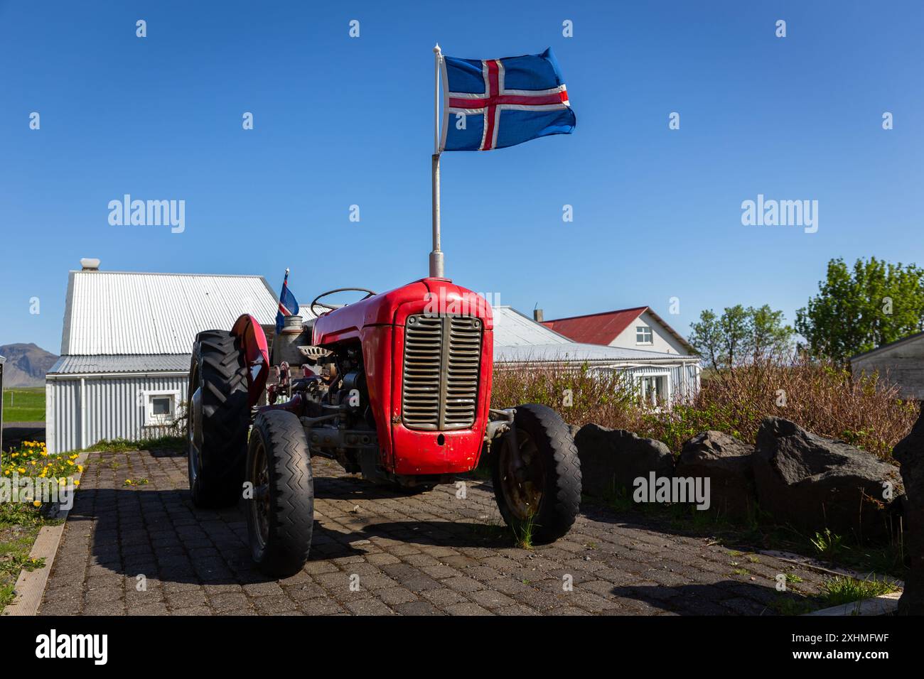 Vecchio trattore agricolo rosso con bandiera nazionale islandese in cima, parcheggiato in un'azienda agricola in Islanda, nessuno. Foto Stock