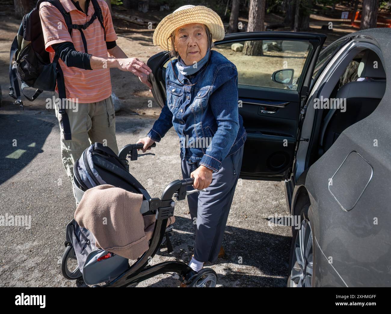 Donna anziana che scende da un'auto e cammina con un camminatore. Mani che tengono aperta la porta dell'auto. Foto Stock