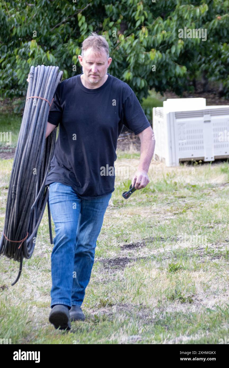Uomo che trasporta una grande bobina di tubi all'aperto Foto Stock