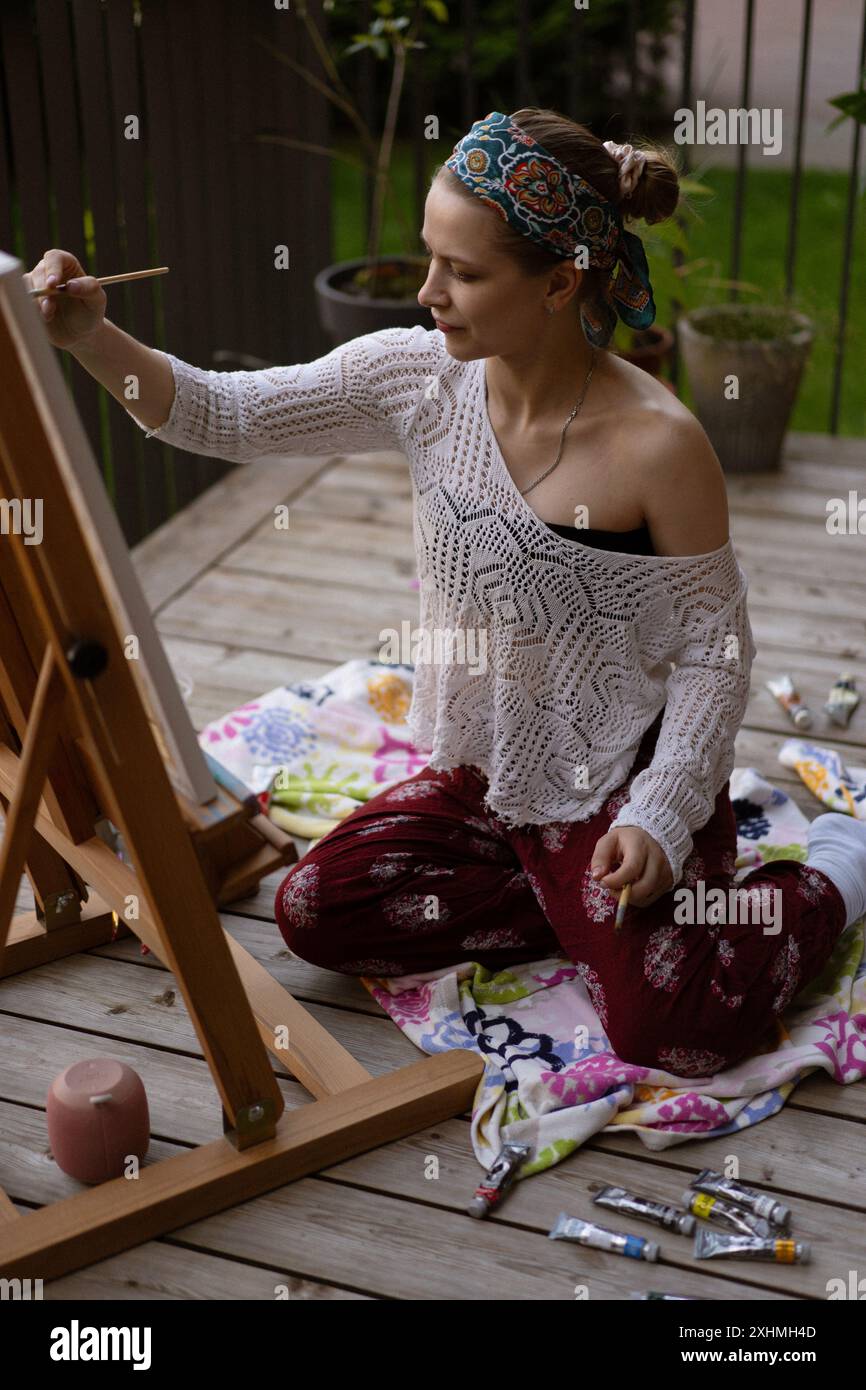 Una donna artista dipinge un quadro su un cavalletto. Foto Stock