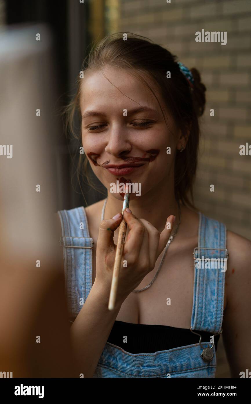 La donna artista le dipinge un baffo sul viso Foto Stock