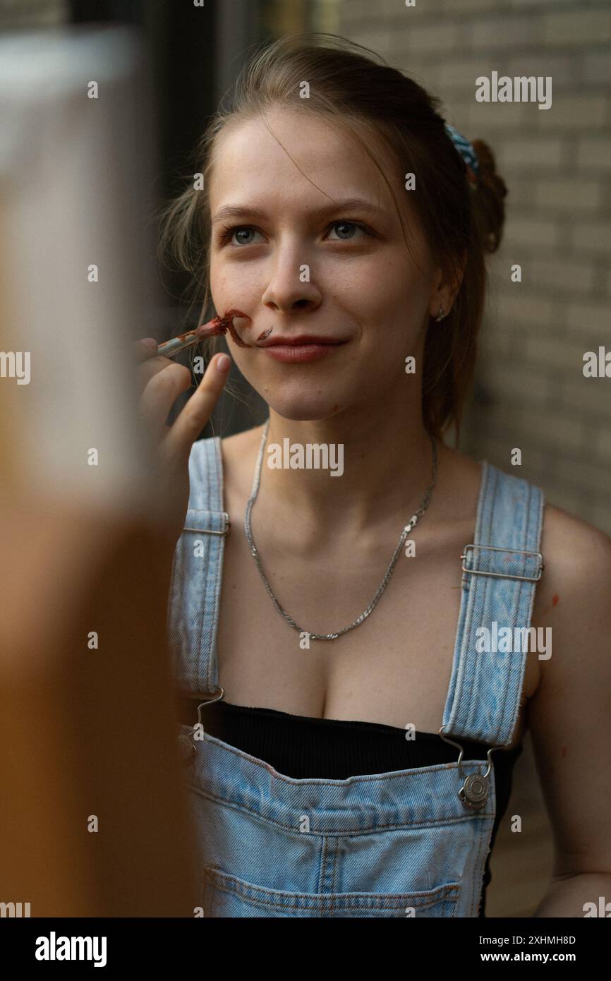 La donna artista le dipinge un baffo sul viso. Foto Stock