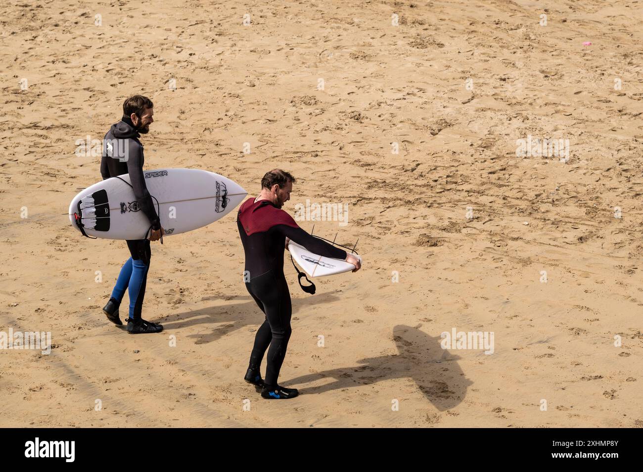 Due amici surfisti che portano le loro tavole da surf camminano lungo Towan Beach a Newquay, in Cornovaglia, nel Regno Unito. Foto Stock