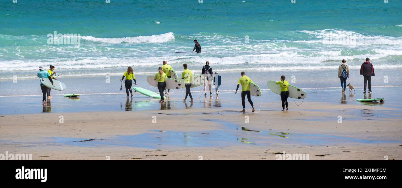 Un'immagine panoramica di un istruttore di surf della Escape Surf School e di un gruppo di principianti che camminano in mare per una lezione di surf a Towan Beach Foto Stock