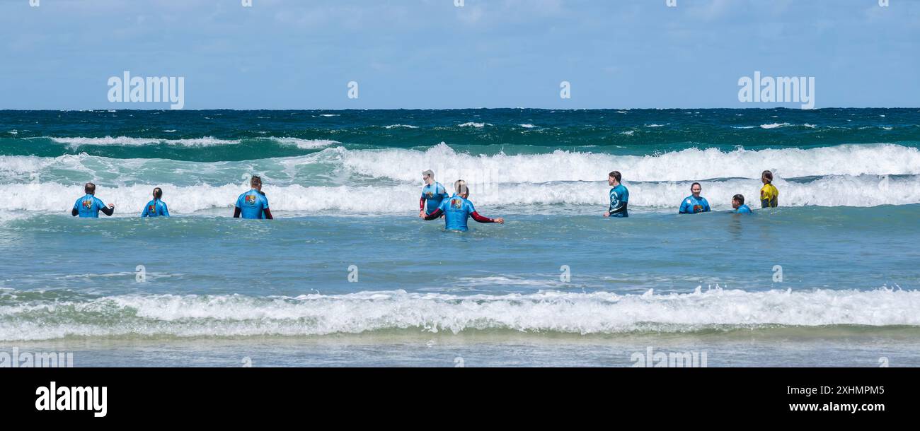 Un'immagine panoramica di un gruppo di vacanzieri che hanno una lezione di surf alla spiaggia di Towan a Newquay, in Cornovaglia nel Regno Unito. Foto Stock