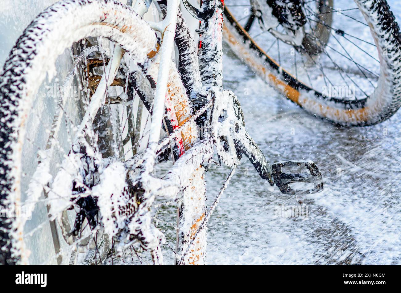 La bici è ricoperta di schiuma bianca. Lavare la bicicletta con getto di schiuma all'autolavaggio. Self-service. Primo piano Foto Stock