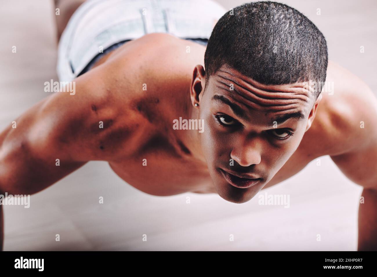 Uomo con uno sguardo concentrato, che fa push-up e mostra un corpo tonificato. I suoi capelli corti e la sua intensa concentrazione sottolineano il suo impegno nel mantenere la fiaba Foto Stock