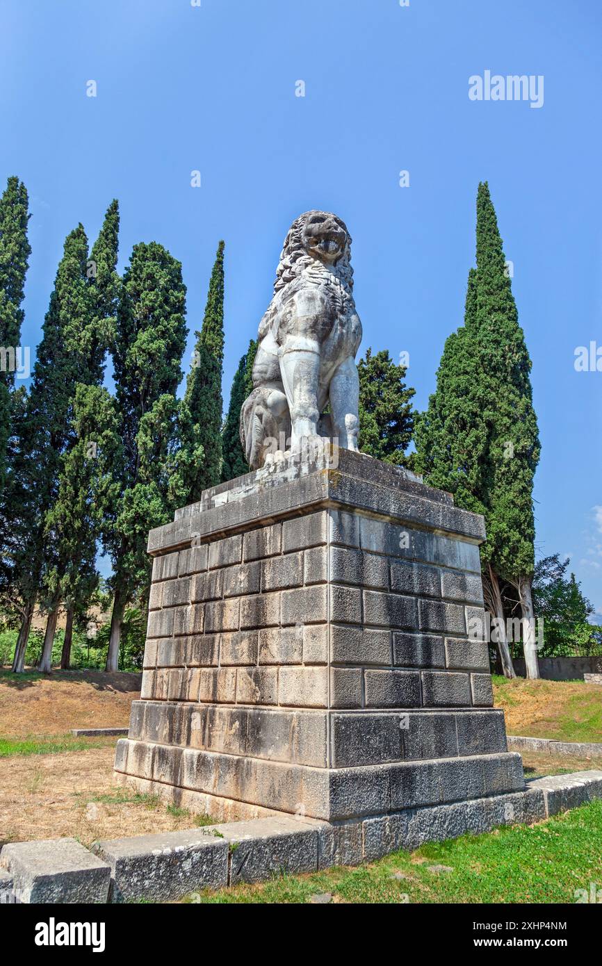 Il Leone di Chaeronea, un antico monumento in marmo in Beozia, Grecia, che si erge maestosamente contro un cielo blu e circondato da lussureggianti cipressi. Foto Stock