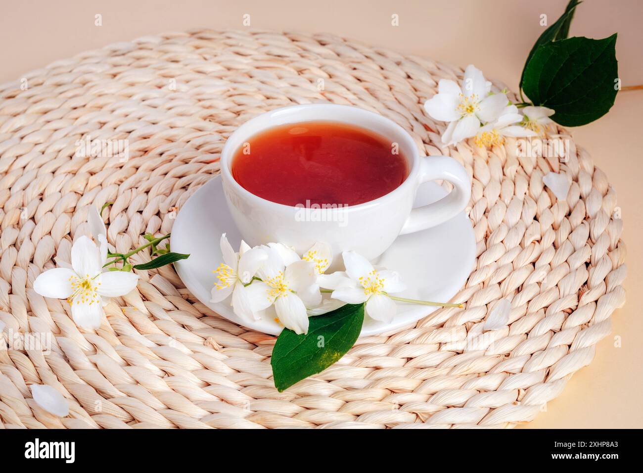Una tazza di tè al gelsomino su un tappeto di vimini con fiori di gelsomino. Vista dall'alto. Foto Stock