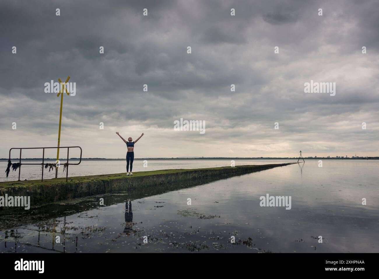 Donna sportiva con le braccia sollevate che si allena con l'acqua e un cielo spettacolare. Allontanarsi da tutto Foto Stock