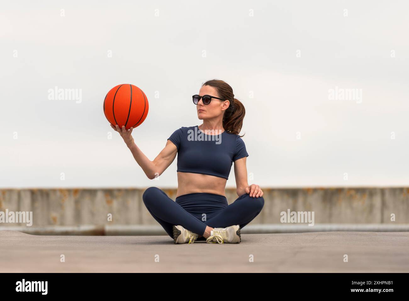 Fit donna sportiva seduta a gambe incrociate con un concetto di basket, sport e fitness. Foto Stock