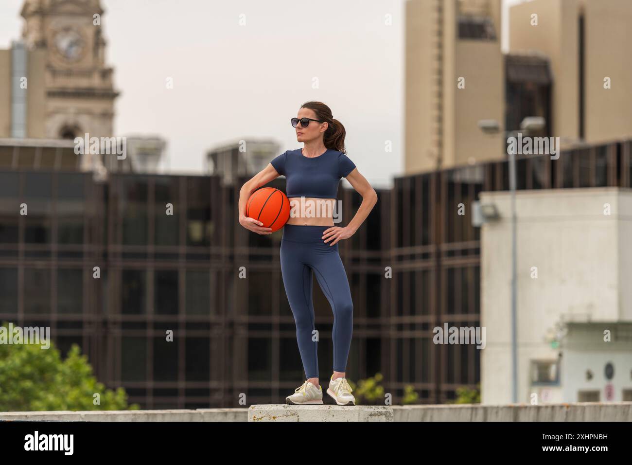 donna che tiene un pallacanestro all'aperto, in città, in attesa di una partita Foto Stock