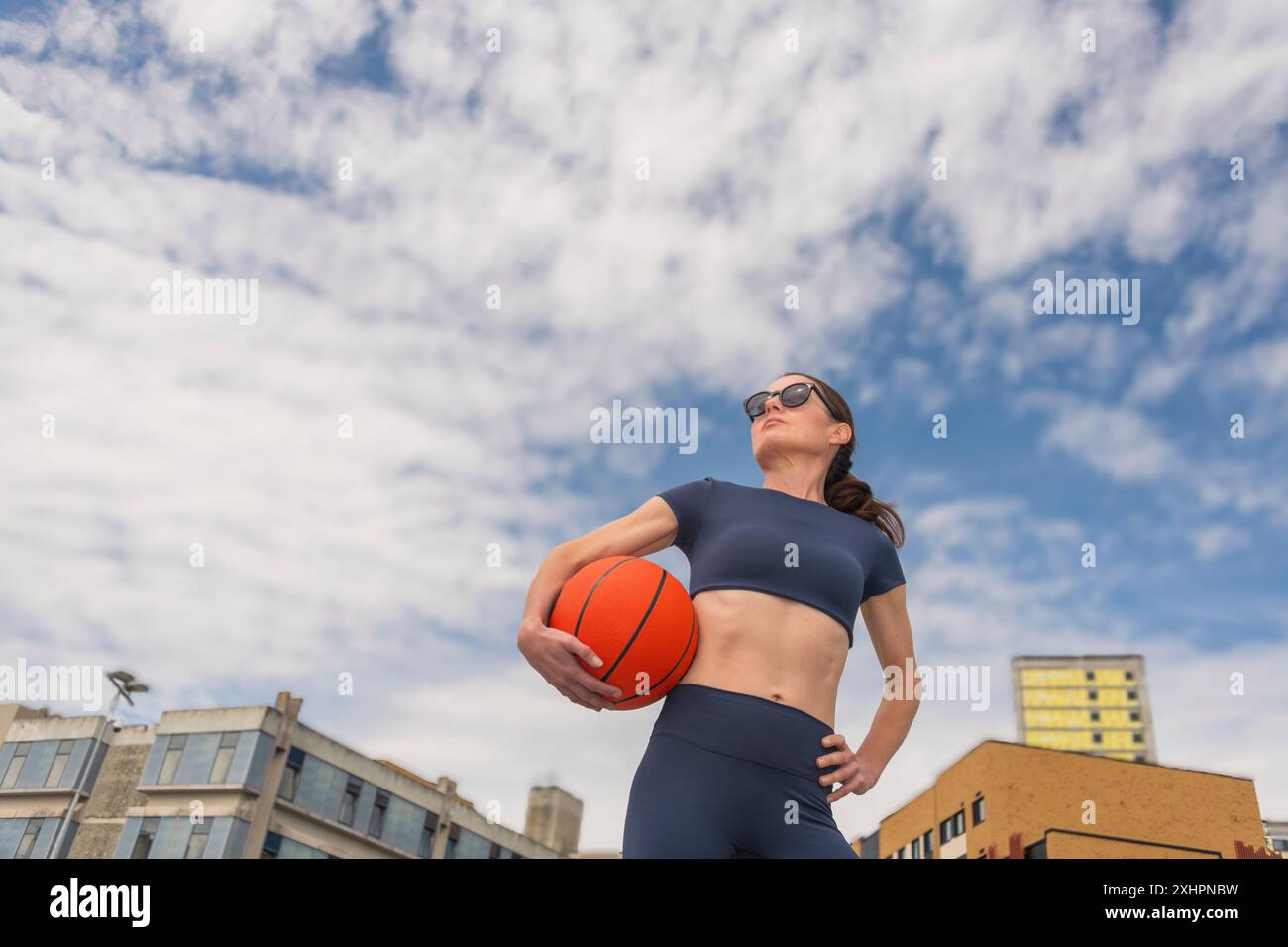 donna che tiene un pallacanestro all'aperto, sfondo urbano, Foto Stock