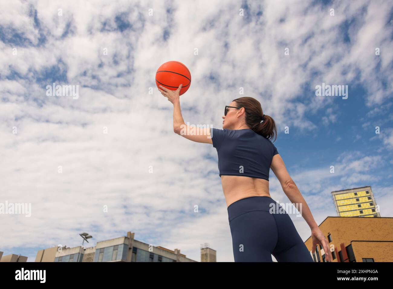 Vista posteriore, donna che tiene in mano un pallacanestro all'aperto, sfondo urbano, scatto, visuale ad angolo basso Foto Stock