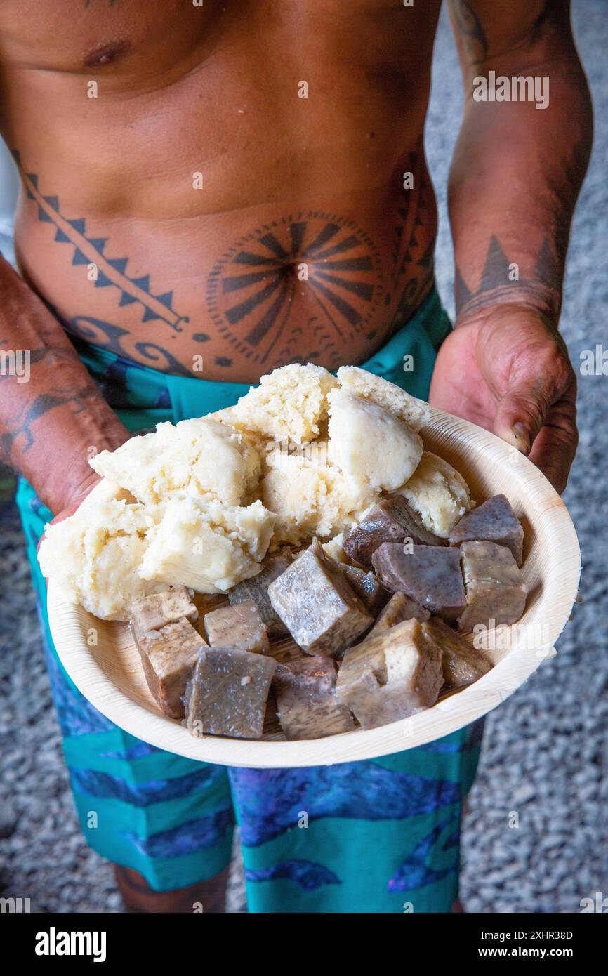 Polinesia francese, isola di Tahiti, polinesiana tatuata con un piatto di taro e pane di cocco in un piatto Foto Stock