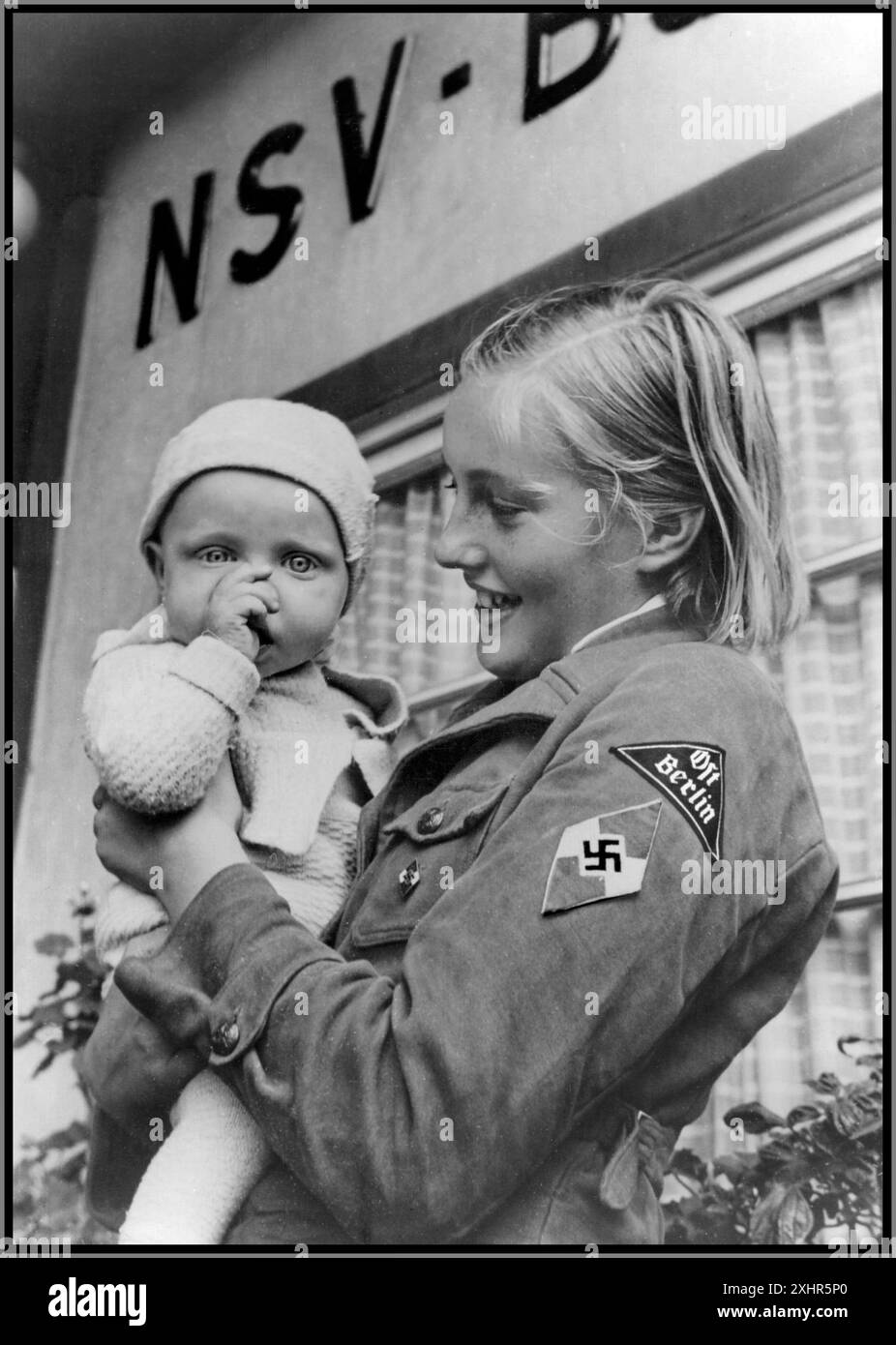 Immagine della Propaganda della Germania nazista del 1930 di una ragazza ariana bionda BDM in uniforme con il distintivo Swastika e il distintivo del braccio di Ost Berlin 1939 fuori dall'ufficio del benessere dei popoli nazionalsocialisti del terzo Reich "NSV" Berlino Germania nazista. La Lega delle ragazze tedesche (in tedesco: Bund Deutscher Mädel, abbreviato in BDM) era l'ala femminile del movimento giovanile del partito nazista, la Gioventù hitleriana. Era l'unica organizzazione legale femminile giovanile nella Germania nazista. Foto Stock