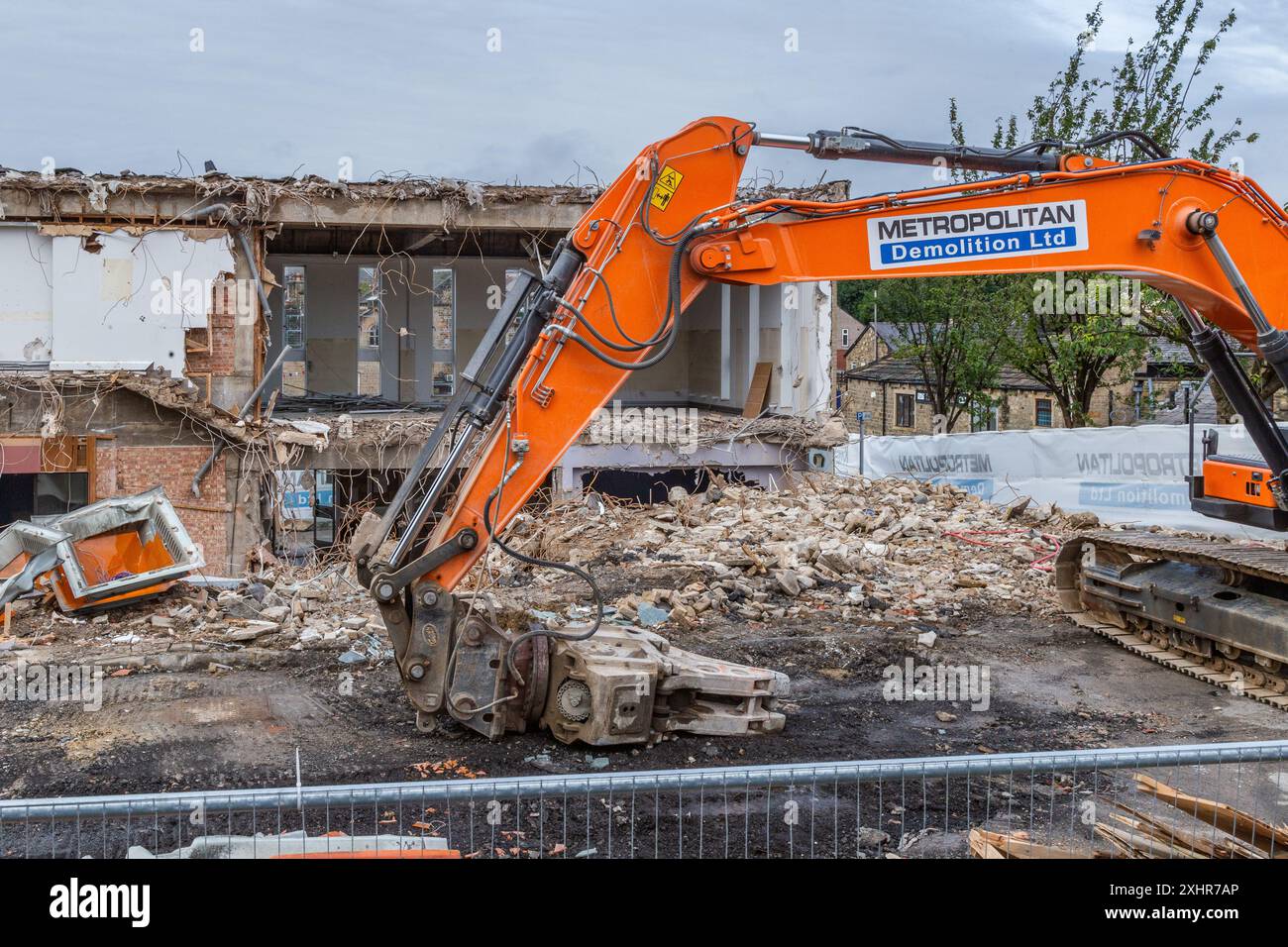 Un escavatore per demolizione al lavoro nel processo di demolizione (demolizione) Baildon Library e Ian Clough Hall (Bradford Council Buildings). Foto Stock