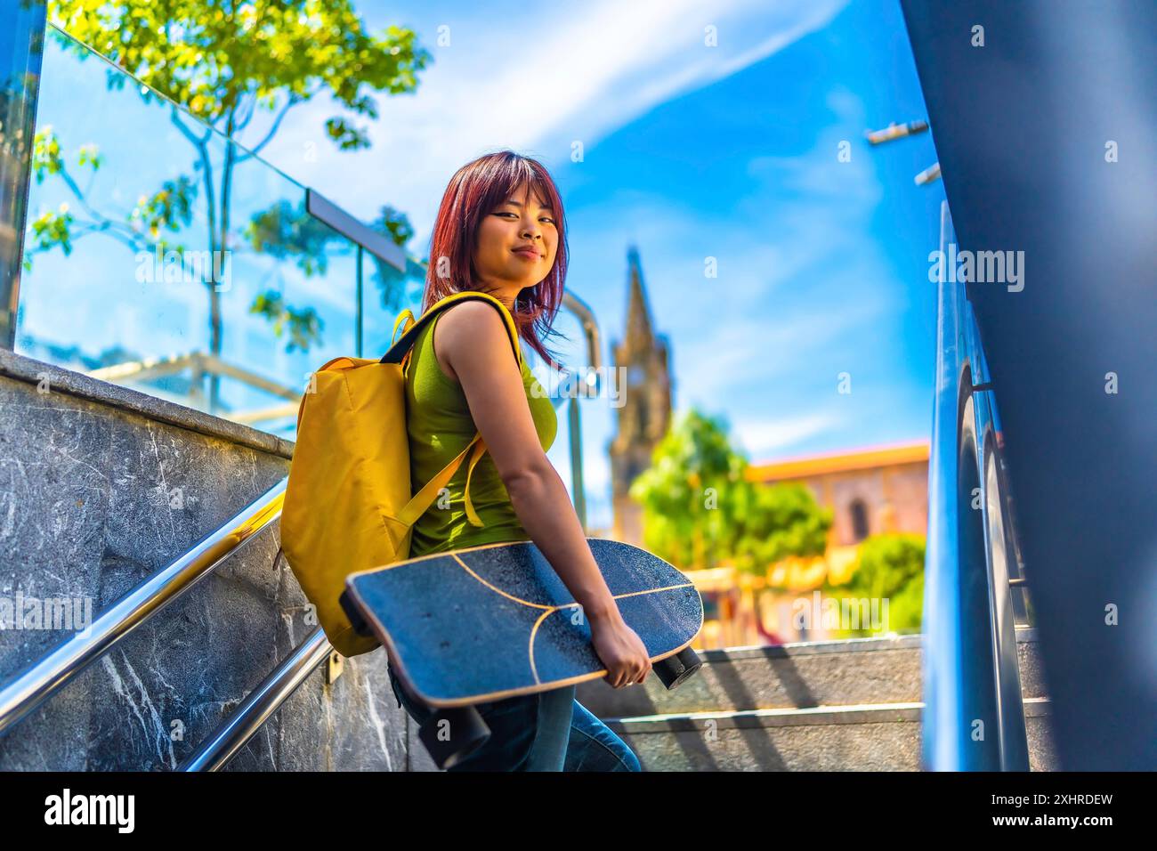 Giovane pattinatrice asiatica che guarda sorridere alla macchina fotografica salendo le scale della città Foto Stock