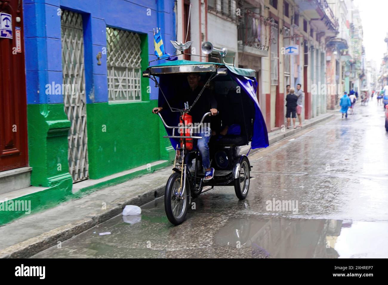 L'Avana, Cuba, l'America centrale, uomo che cavalca un risciò su una strada bagnata in un ambiente urbano Foto Stock