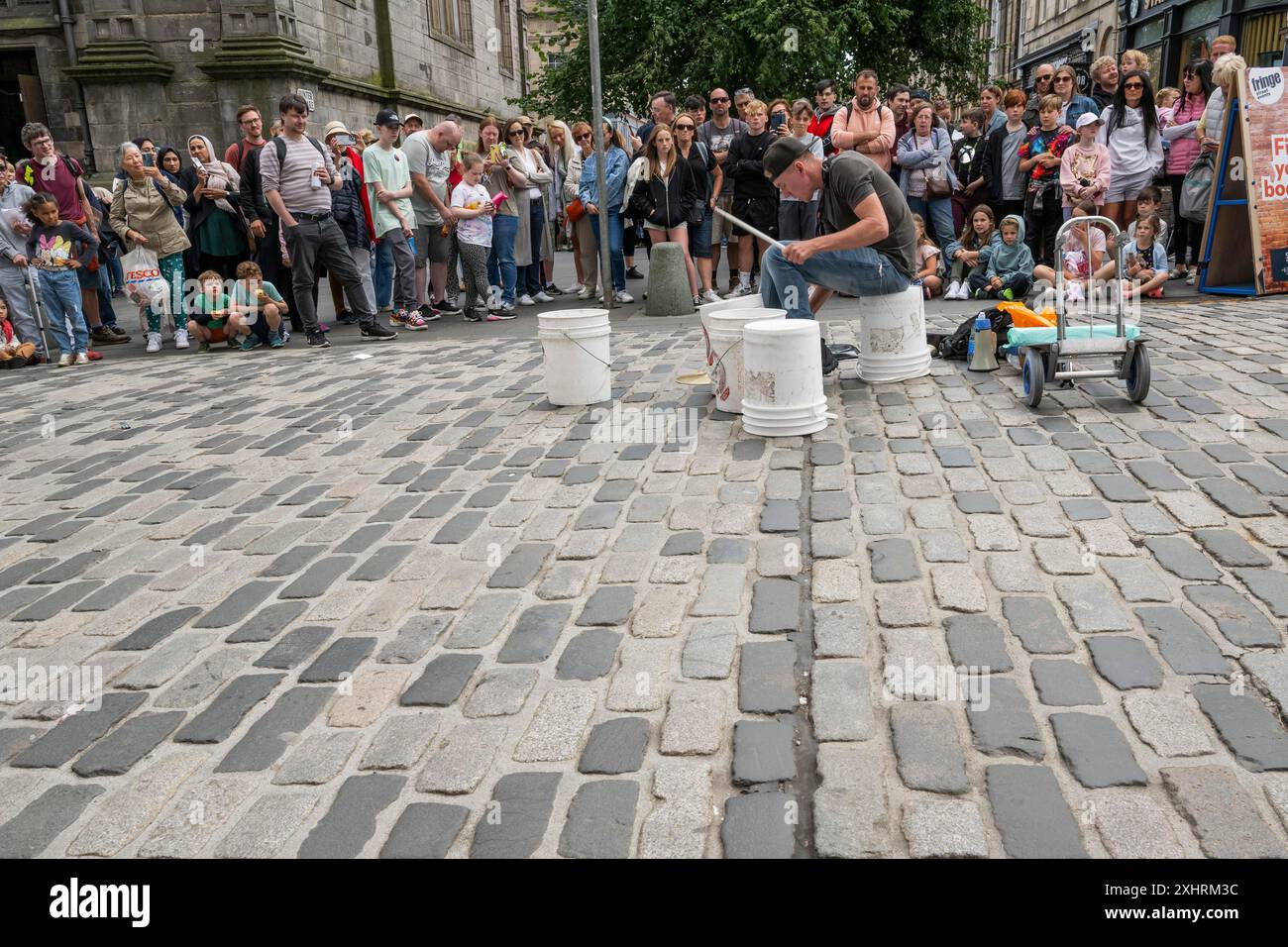 Musicista di strada circondato da spettatori che suonano su secchi vuoti, il più grande festival culturale del mondo The Fringe, High Street, Edimburgo, Scozia Foto Stock