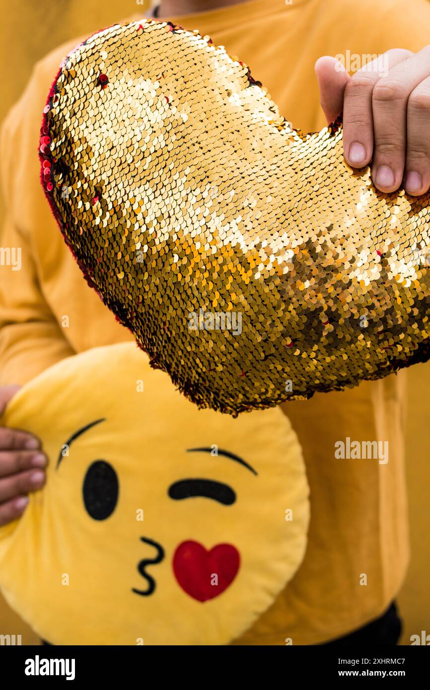 Uno shot verticale di una persona che tiene in mano un cuscino a forma di cuore e un cuscino emoji Foto Stock