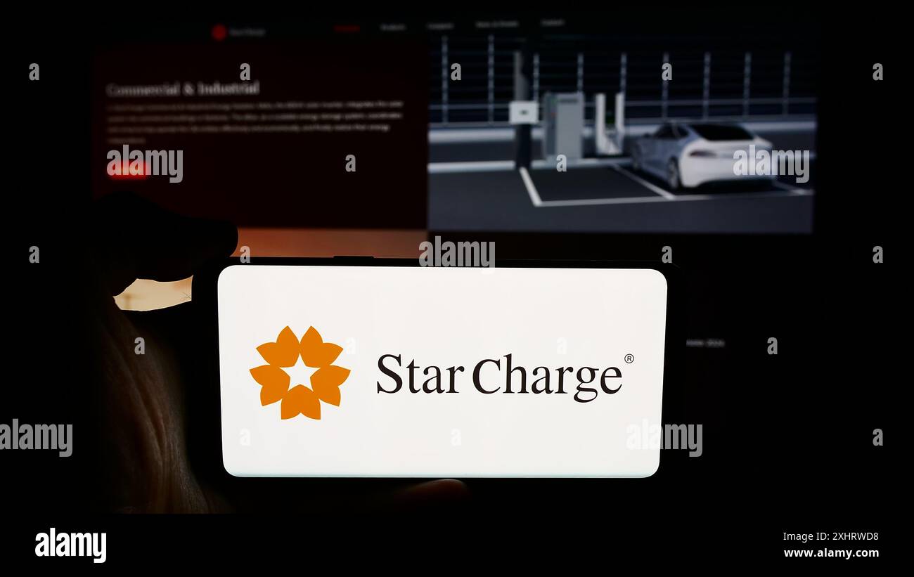 Persona che possiede un cellulare con il logo della società di ricarica per veicoli elettrici di Singapore Star Charge davanti alla pagina Web. Mettere a fuoco il display del telefono. Foto Stock