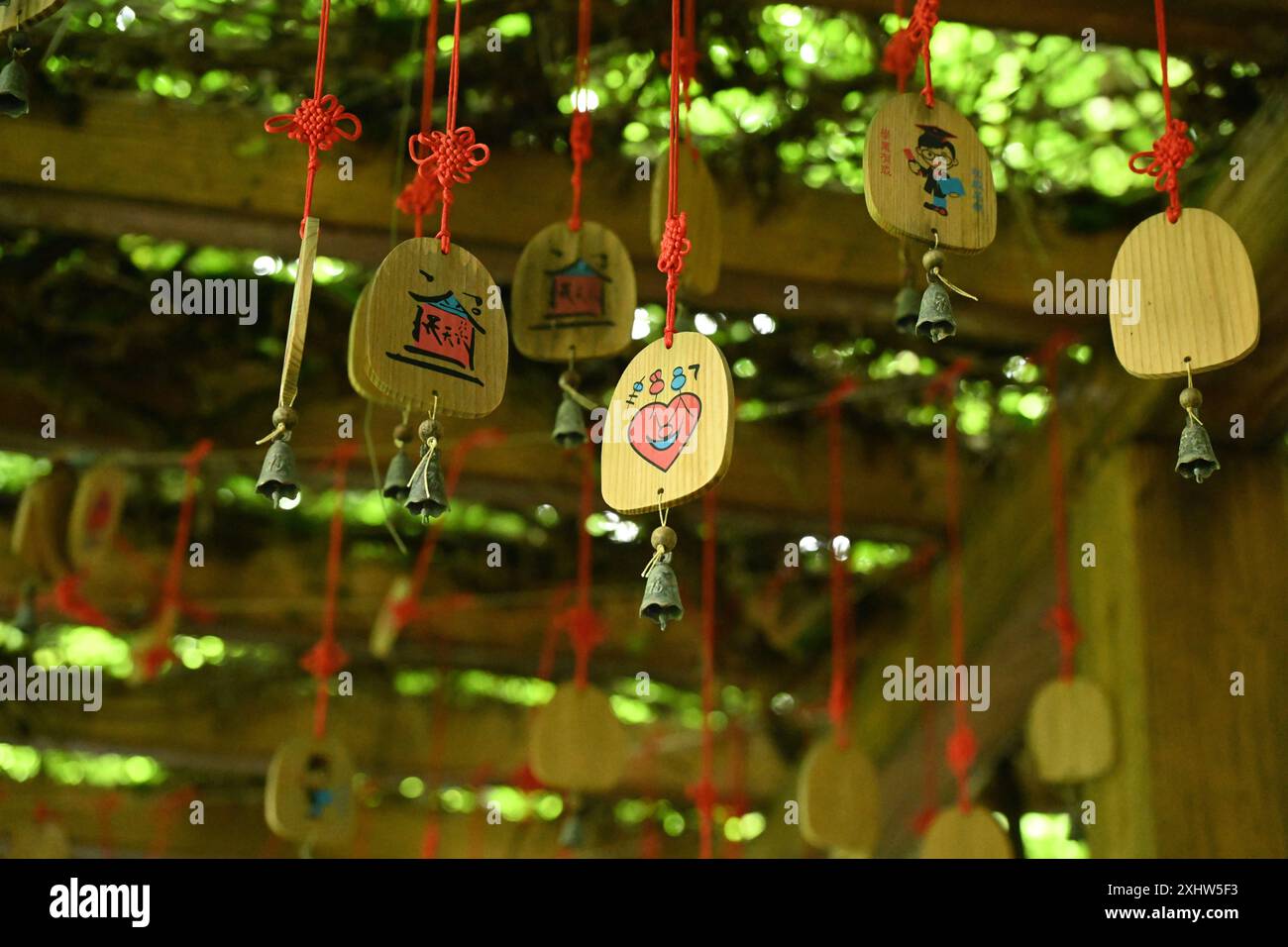 Un gruppo di targhe di legno, ciascuna legata con una corda rossa e adornata con vari simboli e caratteri. Foto Stock