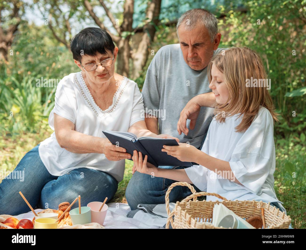 La famiglia trascorre del tempo insieme a un picnic. Nonni e nipoti che leggono un libro durante un picnic estivo Foto Stock