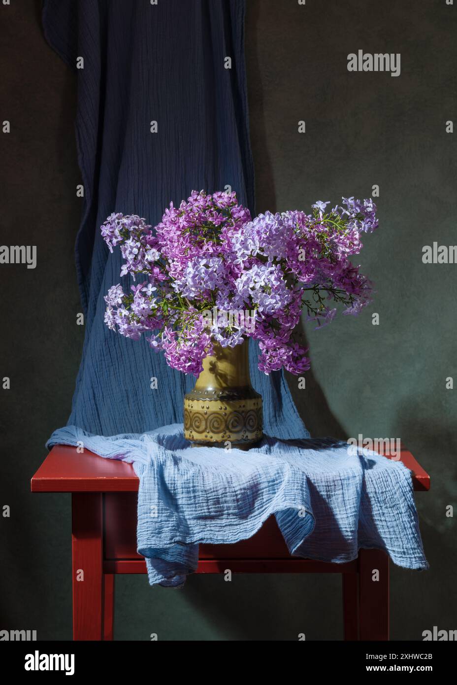 Bouquet di fiori lilla in vaso verde su un tavolo di legno rosso. Natura morta Foto Stock
