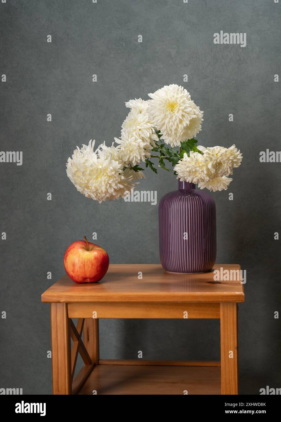 Molti fiori bianchi. Bouquet di Ascire bianche in un vaso viola su un tavolo di legno. C'è una mela rossa accanto ad essa. Sfondo grigio. Vitamine. Salute. Foto Stock