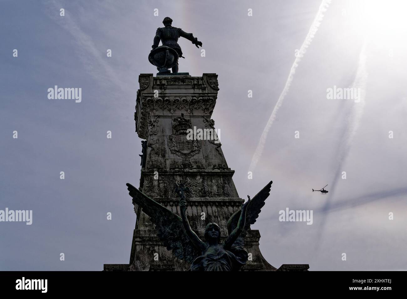 La silhouette del navigatore Infante D. Henrique si erge contro un sole luminoso in un cielo blu sbiadito, con un elicottero che vola sopra Foto Stock