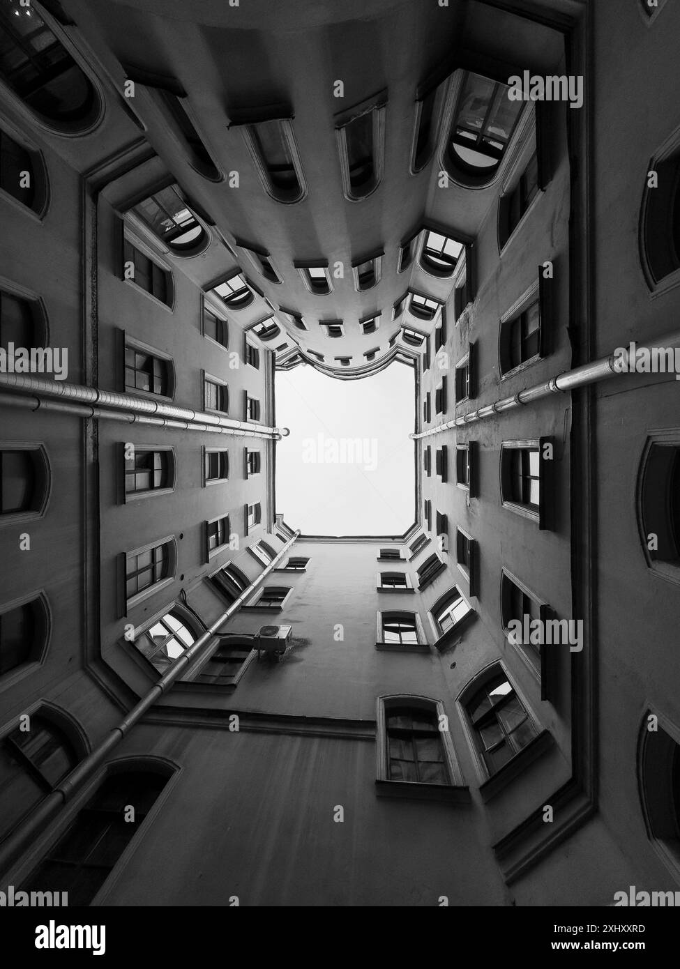 Foto in bianco e nero per catturare una prospettiva unica che guarda verso il cortile interno di un edificio. La geometria architettonica e il design urbano creano un effetto visivo sorprendente. Foto Stock